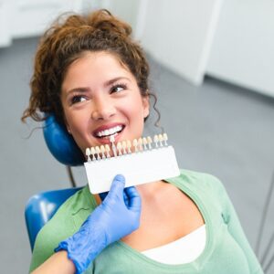 Professional dentist matching patient's teeth color with palette in modern stomatology clinic.