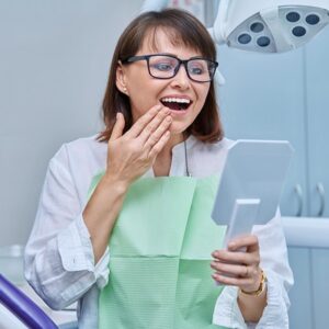 Middle-aged female in dental office looking in mirror.