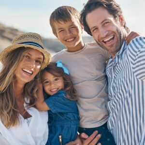 Affectionate couple carrying their two children and posing for a selfie on the beach. Parents are happy after teeth whitening treatment.
